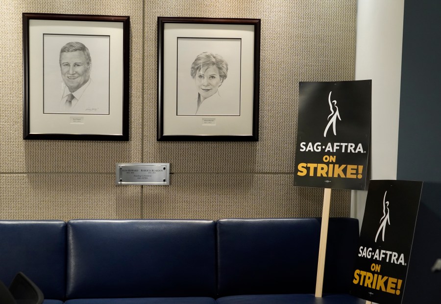 Portraits of SAG-AFTRA founding co-presidents Ken Howard and Roberta Reardon hang next to strike signage following a press conference announcing a strike by The Screen Actors Guild-American Federation of Television and Radio Artists on Thursday, July, 13, 2023, in Los Angeles. This marks the first time since 1960 that actors and writers will picket film and television productions at the same time. (AP Photo/Chris Pizzello)