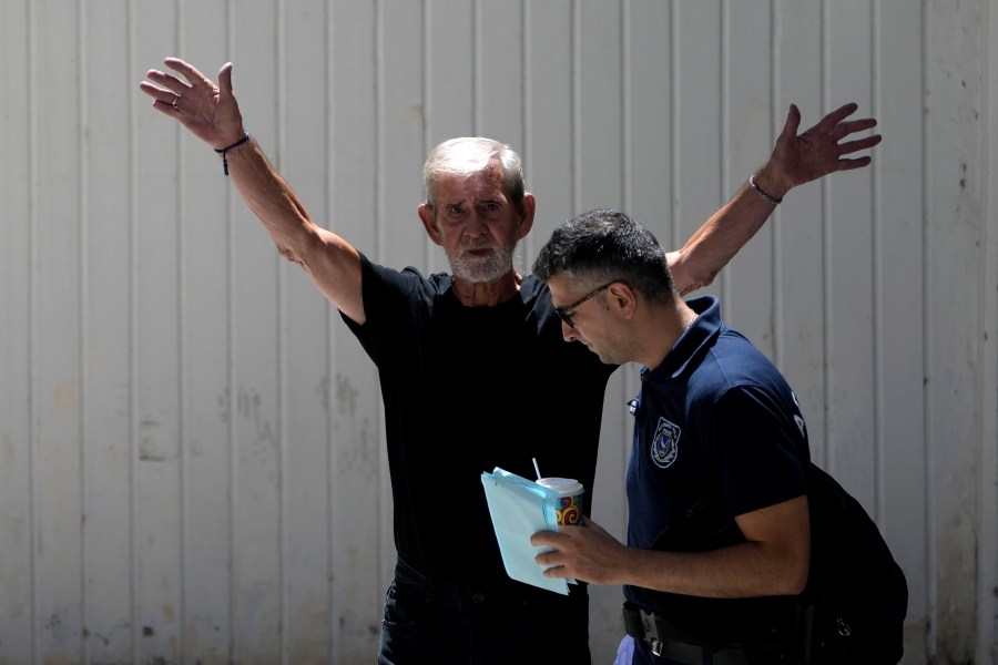 A police officer escorts the Briton David Hunter from the grounds of the courthouse complex after a trial on a premeditated murder charge in the death of his wife, in Paphos, Cyprus, Friday, July 21, 2023. A Cyprus court has found a British man who killed his ailing wife in their home guilty of manslaughter, saying that the prosecution didn't prove beyond reasonable doubt that the 76-year-old man committed premeditated murder. (AP Photo/Petros Karadjias)