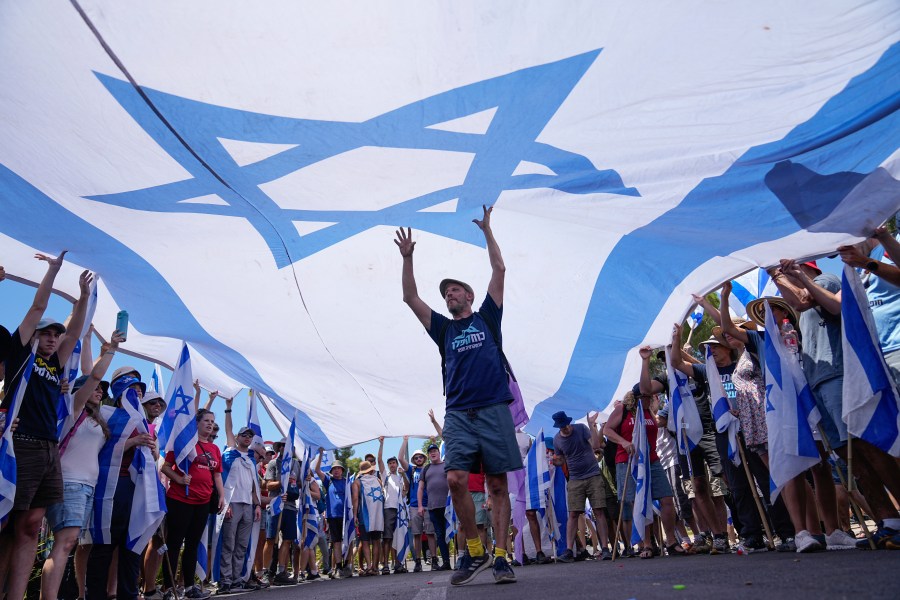 Demonstrators wave a large Israeli flag during a protest against plans by Prime Minister Benjamin Netanyahu's government to overhaul the judicial system, outside the Knesset, Israel's parliament, in Jerusalem, Monday, July 24, 2023. The demonstration came hours before parliament is expected to vote on a key part of the plan. (AP Photo/Ohad Zwigenberg)