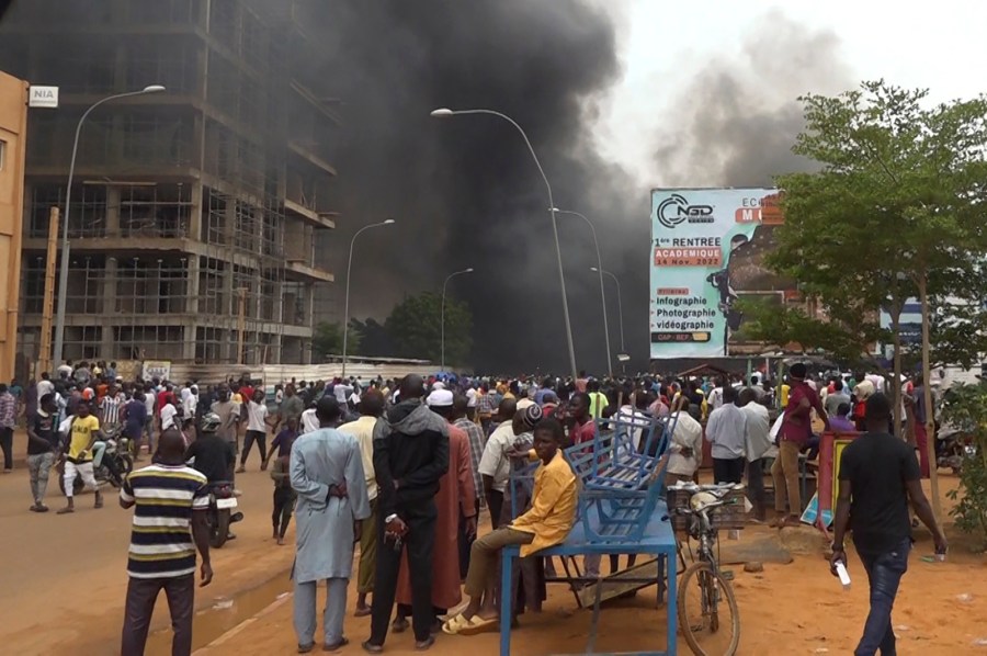 With the headquarters of the ruling party burning in the back, supporters of mutinous soldiers demonstrate in Niamey, Niger, Thursday, July 27 2023. Governing bodies in Africa condemned what they characterized as a coup attempt Wednesday against Niger's President Mohamed Bazoum, after members of the presidential guard declared they had seized power in a coup over the West African country's deteriorating security situation. (AP Photo/Fatahoulaye Hassane Midou)