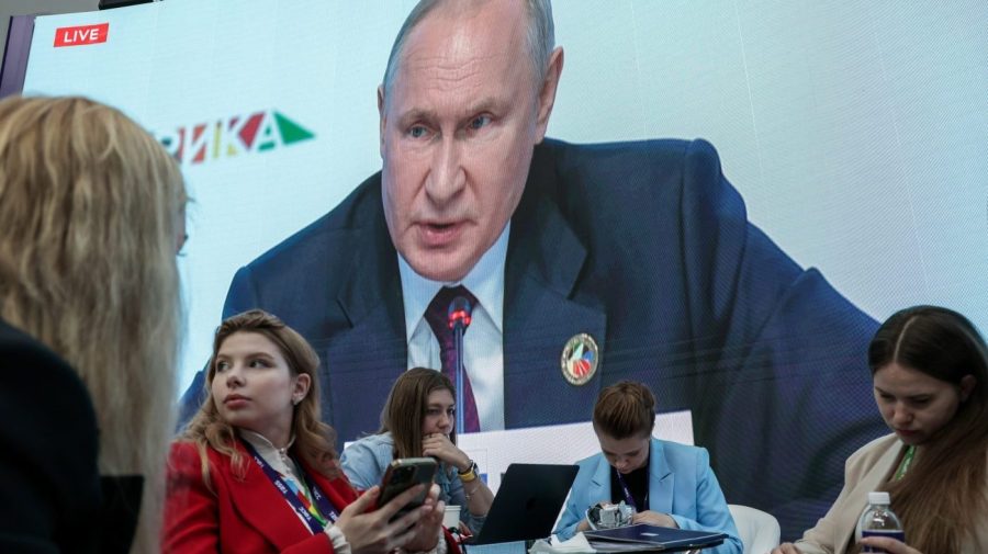 People sit near a TV screen broadcasting Russian President Vladimir Putin's speech during a plenary session at the Russia Africa Summit in St. Petersburg, Russia, Friday, July 28, 2023. (Kirill Kukhmar/TASS Host Photo Agency Pool Photo via AP)