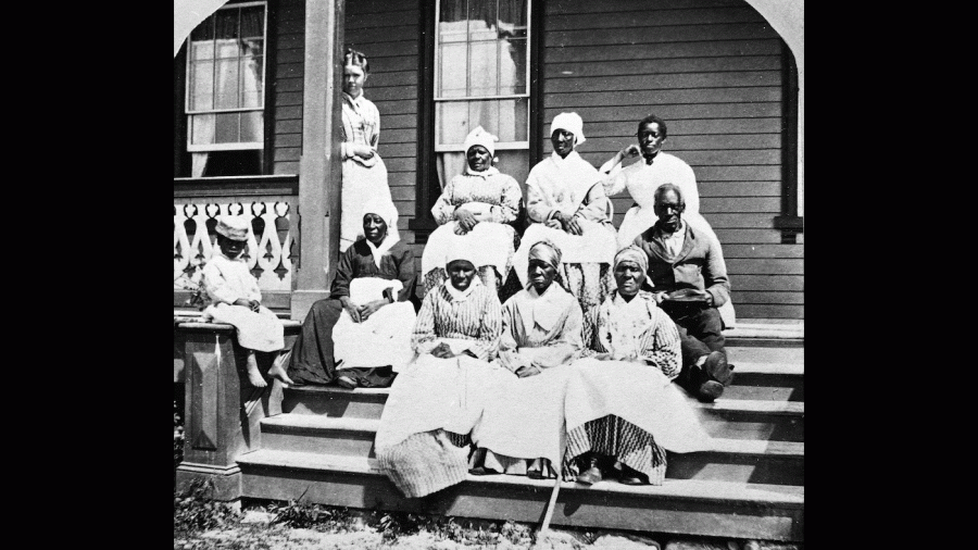 A group of women and a man, presumably enslaved, sit on the steps of the Florida Club, St. Augustine, Florida, mid 19th Century. A white woman, possibly a manager or overseer, stands behind them to the left and a child sits on the newel post. (Photo by Hulton Archive/Getty Images)