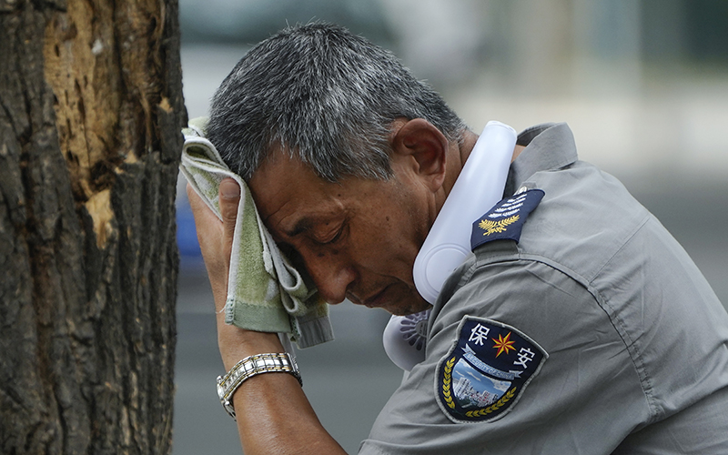 A security guard wearing an electric fan on his neck wipes off sweat on a hot day