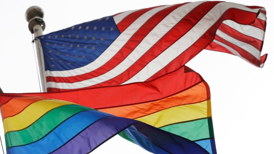 An American flag and rainbow flag fly in the wind.