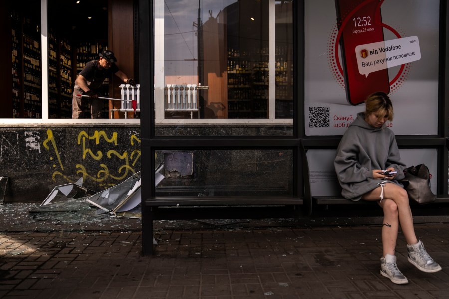 A commuter waits for a bus in front of a liquor store damaged in Russian drone attacks in Kyiv, Ukraine, Wednesday, Aug. 2, 2023. (AP Photo/Jae C. Hong)