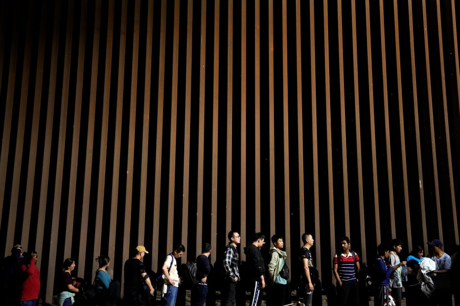 FILE - People line up against a border wall as they wait to apply for asylum after crossing the border from Mexico, July 11, 2023, near Yuma, Ariz. An appeals court Thursday, Aug. 3, allowed a rule restricting asylum at the southern border to stay in place. The decision is a major win for the Biden administration, which had argued that the rule was integral to its efforts to maintain order along the U.S.-Mexico border. (AP Photo/Gregory Bull, File)