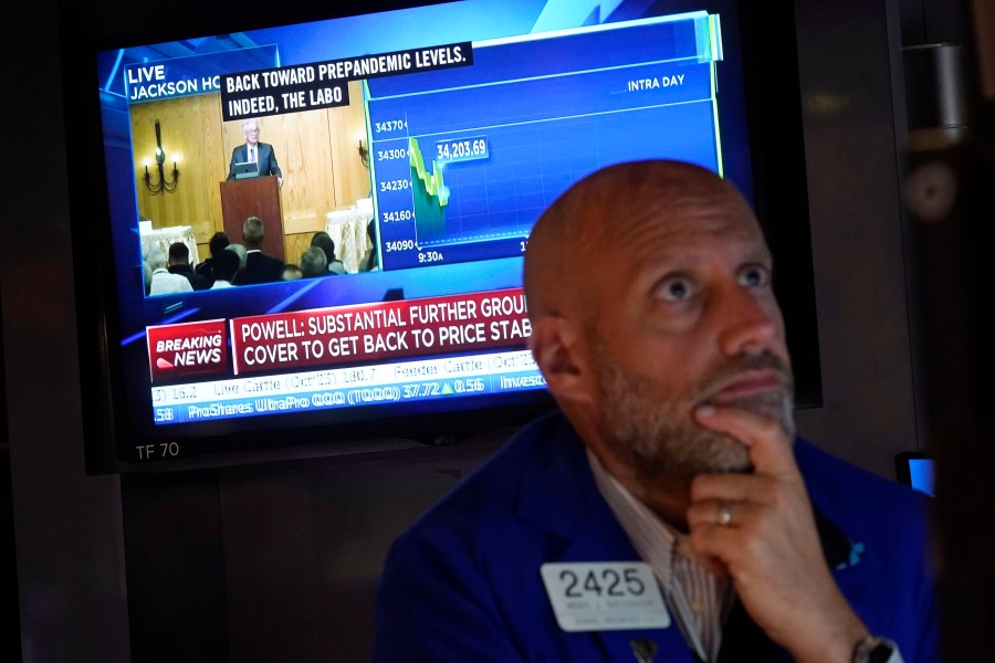 Specialist Meric Greenbaum works at his post on the floor of the New York Stock Exchange, Friday, Aug. 25, 2023, as Federal Reserve Chair Jerome Powell's speech shows on a television screen. Stocks are holding on to gains after Powell said more rate hikes could be on the way to continue the Fed's fight against inflation. (AP Photo/Richard Drew)