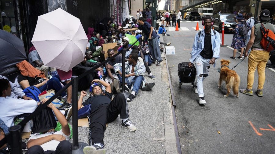 Migrants sit in a queue outside of The Roosevelt Hotel that is being used by the city as temporary housing, Monday, July 31, 2023, in New York.