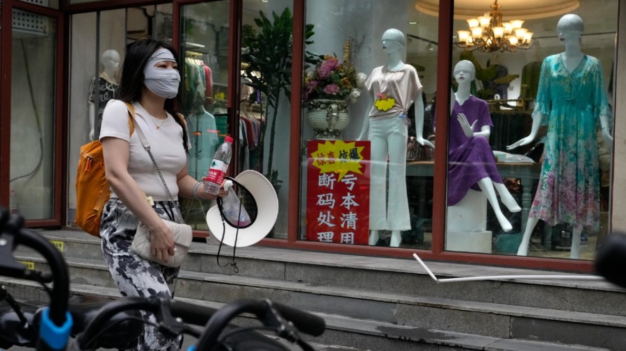 A woman walks past a store with a sign which reads "Clearing at a lost, left-over sizes clearance" at a store in Beijing, Thursday, July 27, 2023. Chinese leader Xi Jinping's government is promising to drag the economy out of a crisis of confidence aggravated by tensions with Washington, wilting exports, job losses and anxiety among foreign companies about an expanded anti-spying law. (AP Photo/Ng Han Guan)