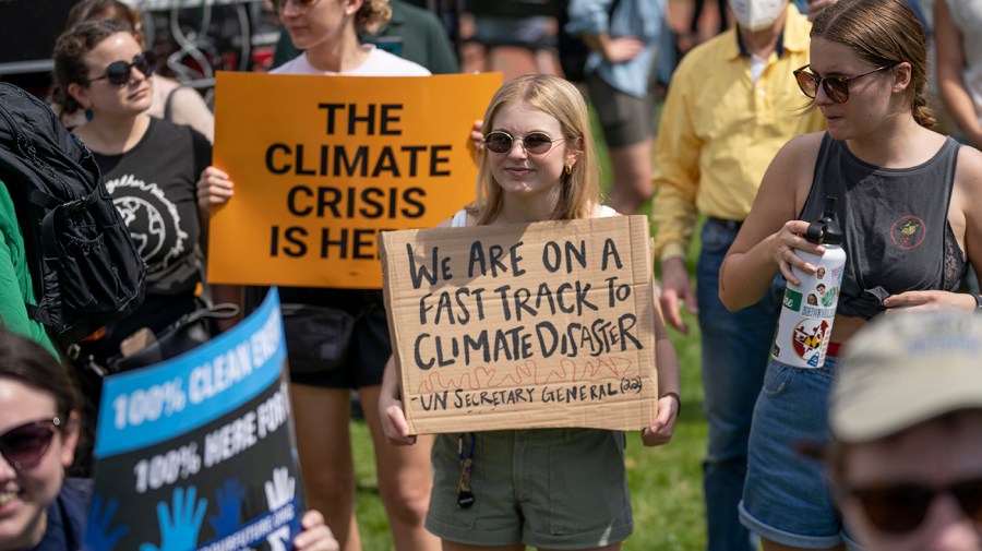 Climate activists congregate with signs; one sign reads "We are on a fast track to climate disaster" and another, colored orange, reads "The climate crisis is here"