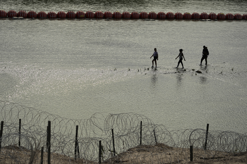 Migrants walk past large buoys