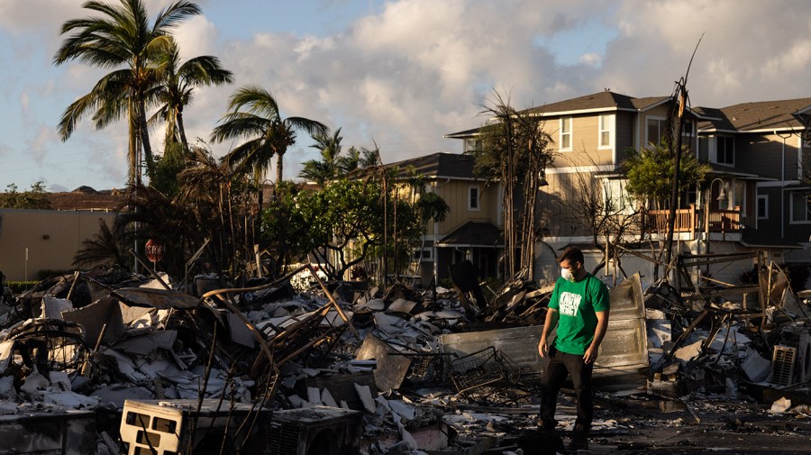 A volunteer stands in the wreckage of a charred apartment complex after a wildfire