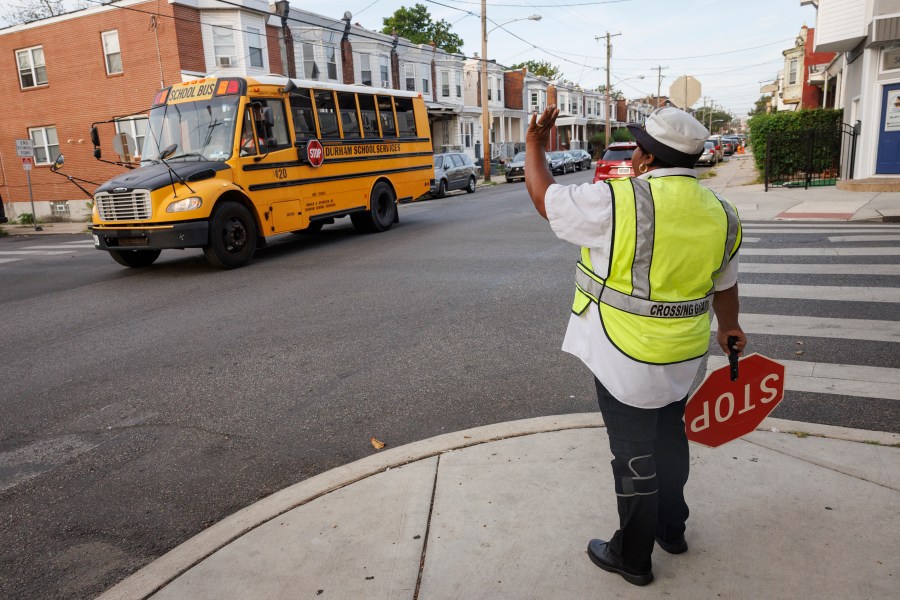 Crossing guard Pamela Lane waves a school bus passing her intersection, Master and N. 57th Street as she crosses students going to Bluford Elementary School, Tuesday, Sept. 5, 2023, in Philadelphia.