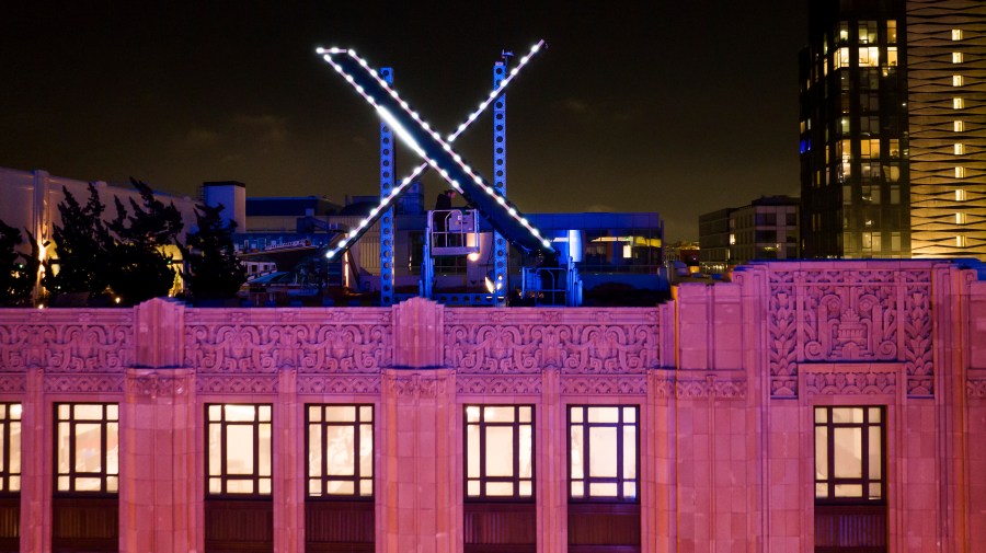 Workers install lighting on an "X" sign atop the company headquarters.