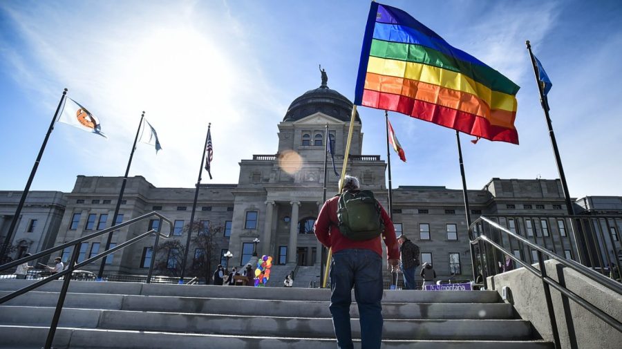 A demonstrators holding a large rainbow pride flag walks up the steps to a gathering at the Montana state Capitol.