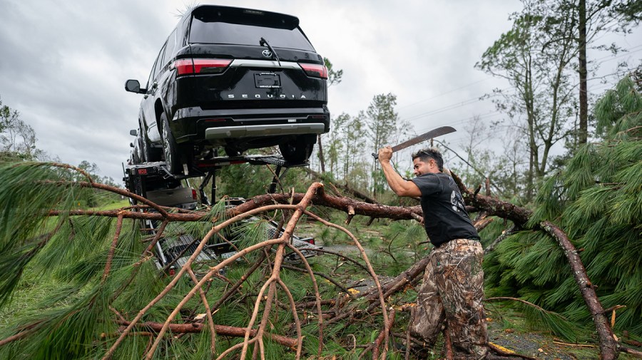 A truck driver uses a machete to clear I-10 of fallen trees and branches