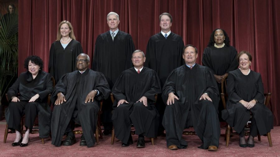 Members of the Supreme Court sit for a group portrait against a red curtain.