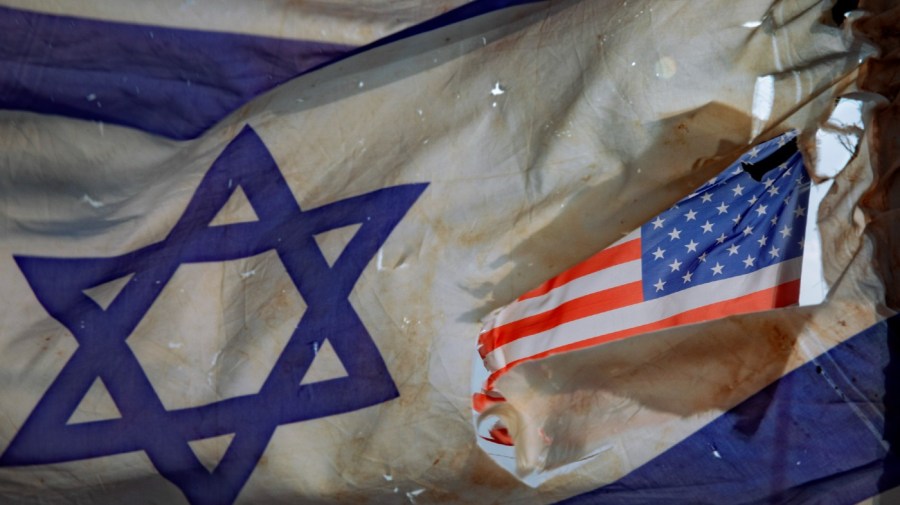 A U.S. flag is seen through a hole torn in an Israel national flag, as they wave in the wind at a horse ranch, near the southern Israeli town of Sderot, Friday, Nov. 20, 2020.