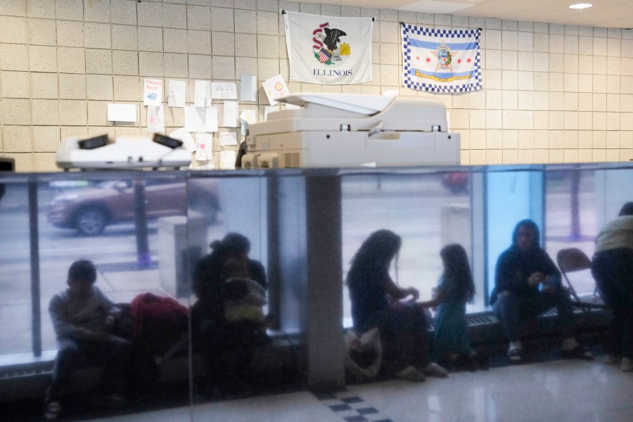 FILE - Immigrants from Venezuela are reflected in a marble wall while taking shelter at the Chicago Police Department's 16th District station on May 1, 2023. Five mayors from around the U.S. want a meeting with President Joe Biden to ask for help controlling the continued arrival of large groups of migrants to their cities. The mayors of Denver, Chicago, Houston, New York and Los Angeles say in a letter to Biden that there has been little to no coordination, support or resources and that is leading to a crisis. (AP Photo/Charles Rex Arbogast, FIle)