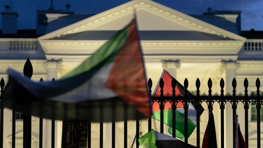 Palestinian flags are seen waving in front of the White House against a darkened sky.