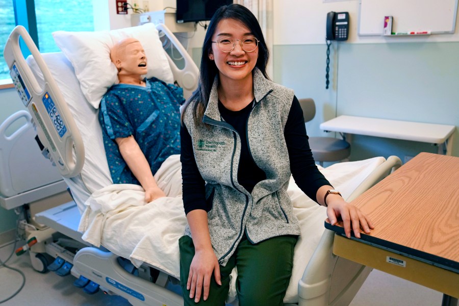 Andy Hoang, a recent nursing graduate, poses with a training mannequin in a patient bedroom training lab at Dartmouth-Hitchcock Medical Center, Tuesday, Dec. 5, 2023, in Lebanon, N.H. Hoang, 23, started to feel dizzy and nauseous during the recent cardiac training session at the hospital and needed help immediately. Instead of practicing chest compressions on a mannequin in the simulated environment of their training, her four colleagues sprung into action and went to work on her. (AP Photo/Charles Krupa)