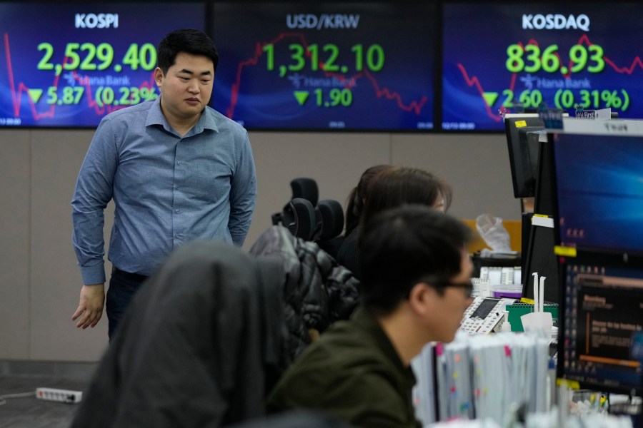 A currency trader passes by the screens showing the Korea Composite Stock Price Index (KOSPI), left, and the foreign exchange rate between U.S. dollar and South Korean won, center, at the foreign exchange dealing room of the KEB Hana Bank headquarters in Seoul, South Korea, Wednesday, Dec. 13, 2023. Asian shares were mixed on Wednesday after Wall Street rose to its highest level since early 2022, slightly below its record high, following a report showing inflation in the United States is behaving pretty much as expected. (AP Photo/Ahn Young-joon)