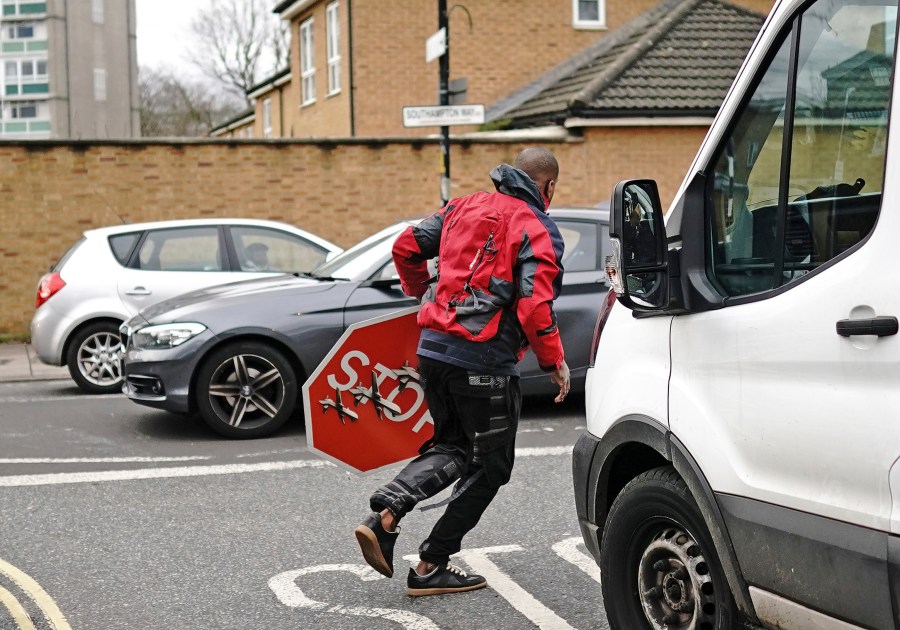 A person removes a piece of art work by Banksy, which shows what looks like three drones on a traffic stop sign, which was unveiled at the intersection of Southampton Way and Commercial Way in Peckham, south east London, Friday Dec. 22, 2023. (Aaron Chown/PA via AP)