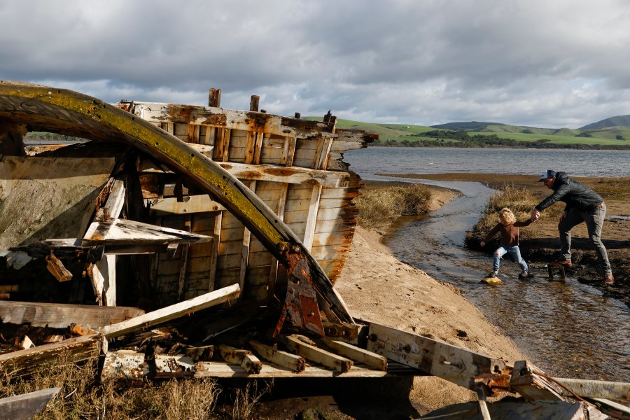 Tourists explore the "Inverness Shipwreck" as it sits in disarray on the shores of Tomales Bay in Inverness, Calif. Wednesday, Jan. 3, 2024. Time is apparently running out for the old wooden boat that became an Instagram star as it rotted on a shoreline north of San Francisco. Recent storms have made a shambles of the forlorn vessel Point Reyes, a landmark that was already deteriorated from the over-attention of visitors to the Marin County coast. (Jessica Christian/San Francisco Chronicle via AP)