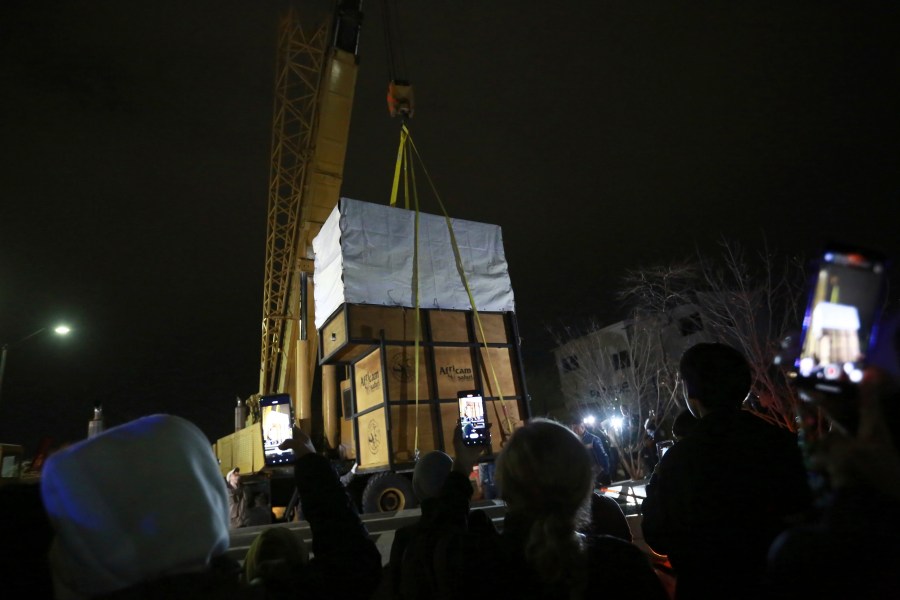 Onlookers take photos of the crate carrying Benito the giraffe as it is loaded for transport at the city-run Central Park zoo in Ciudad Juarez, Mexico, Sunday, Jan. 21, 2024. After a campaign by environmentalists, Benito left Mexico's northern border and its extreme weather conditions Sunday night and headed for a conservation park in central Mexico, where the climate is more akin to his natural habitat and already a home to other giraffes. (AP Photo/Christian Chavez)