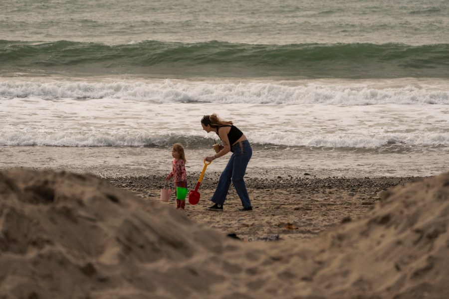 Babysitter Nathalie Miotti plays in the sand with Mia Seth, 2, on the beach behind a protective sand mound ahead of storms in Ventura, Calif., Wednesday, Jan. 31, 2024. (AP Photo/Damian Dovarganes)