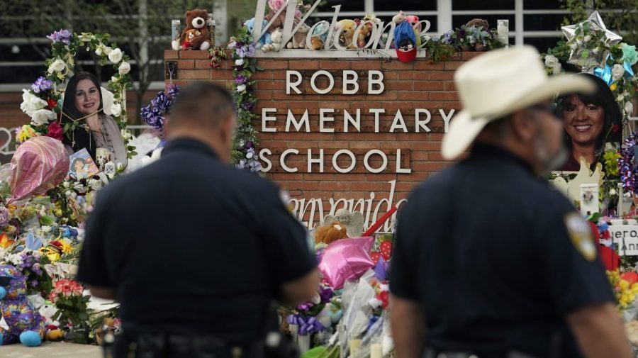 Officers visit a memorial set up around the Robb Elementary School sign.