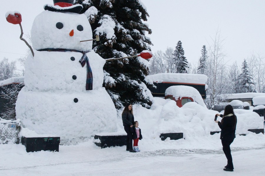 FILE - Nihal Mico takes a photo of her sister-in-law Isil Mico as she poses with her daughter Lorena in front of Snowzilla, a snowman measuring more than 20 feet tall, in Anchorage, Alaska, on Jan. 10, 2024. Much of Alaska has plunged into a deep freeze, with temperatures well below zero and Anchorage seeing some of its coldest temperatures in years as the mayor of the state’s largest city opened warming facilities for those who are homeless or who don't have reliable heating. (AP Photo/Mark Thiessen, File)