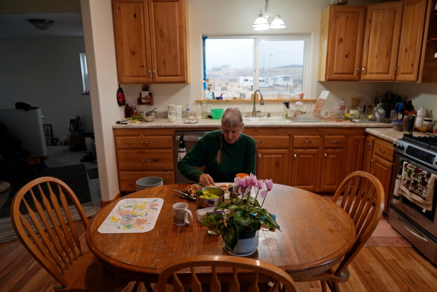 Gayna Salinas eats breakfast in her kitchen Thursday, Jan. 25, 2024, in Green River, Utah, with a view of an abandoned uranium mine behind her. An Australian company and its U.S. subsidiaries are eyeing a nearby area to extract lithium, metal used in electric vehicle batteries. Salinas, whose family farms in the rural community, said she was skeptical about the project's benefits. (AP Photo/Brittany Peterson)