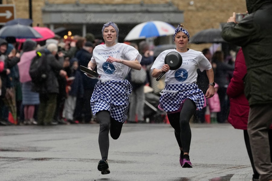 Pancake race winner Kaisa Larkas, right, and second place finisher Eloise Kramer run ahead during the annual Shrove Tuesday trans-Atlantic pancake race in the town of Olney, in Buckinghamshire, England, Tuesday, Feb. 13, 2024. Every year women clad in aprons and head scarves from Olney and the city of Liberal, in Kansas, USA, run their respective legs of the race with pancakes in their pans. According to legend, the Olney race started in 1445 when a harried housewife arrived at church on Shrove Tuesday still clutching her frying pan with a pancake in it. (AP Photo/Kin Cheung)