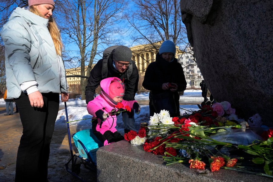 A family pay tribute to Alexei Navalny at the monument, a large boulder from the Solovetsky islands, where the first camp of the Gulag political prison system was established in St. Petersburg, Russia, Sunday, Feb. 18, 2024. Russians across the vast country streamed to ad-hoc memorials with flowers and candles to pay tribute to Alexei Navalny, the most famous Russian opposition leader and the Kremlin's fiercest critic. Russian officials reported that Navalny, 47, died in prison on Friday. (AP Photo/Dmitri Lovetsky)