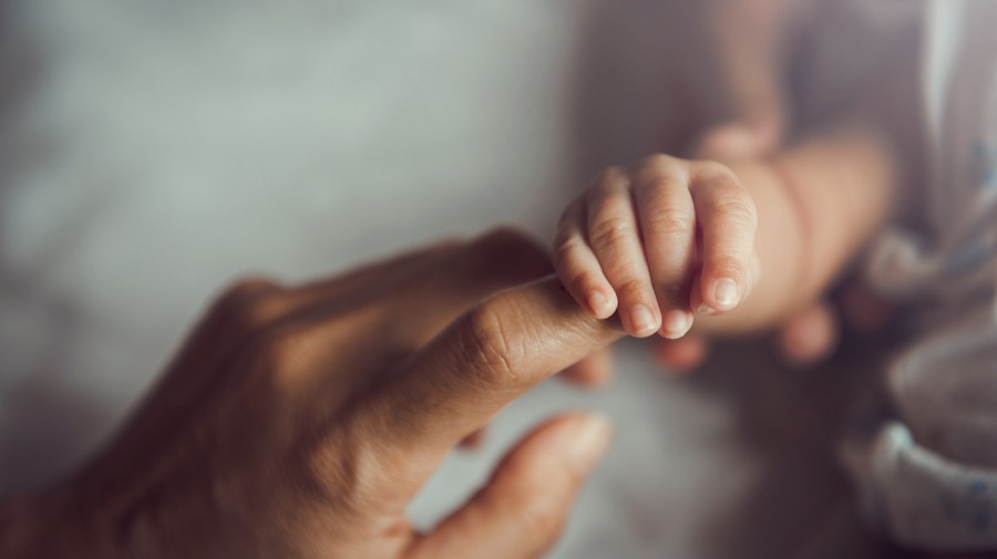 A newborn baby holds a mother's finger.