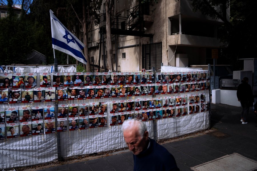 People pass by a fence with photographs of Israelis who are being held hostage in the Gaza Strip by the Hamas militant group, in Ramat Gan, Israel, Thursday, March 7, 2024. (AP Photo/Oded Balilty)