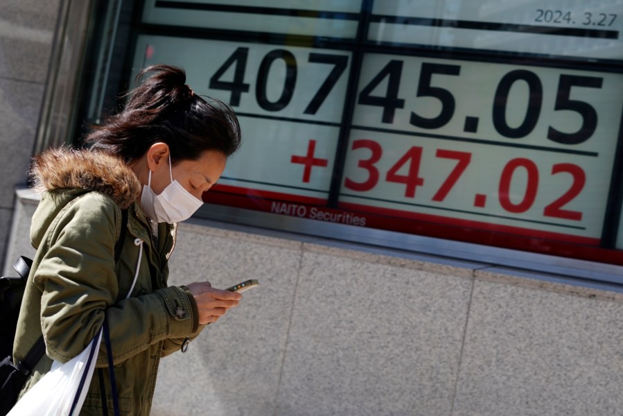 A person walks in front of an electronic stock board showing Japan's Nikkei 225 index at a securities firm Wednesday, March 27, 2024, in Tokyo. Asian shares were mixed on Wednesday after Wall Street slipped a bit further from its record highs. (AP Photo/Eugene Hoshiko)