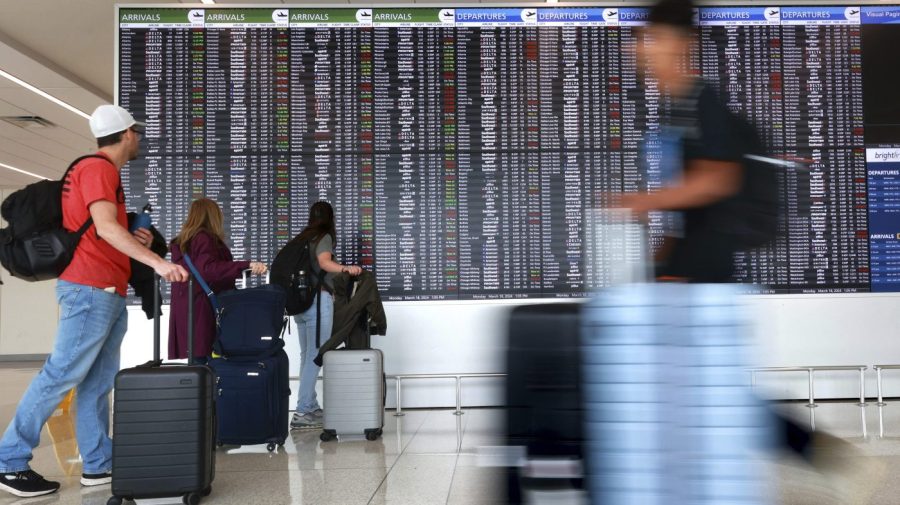 Passengers arrive at the Orlando Airport with a flight information display system in the background.