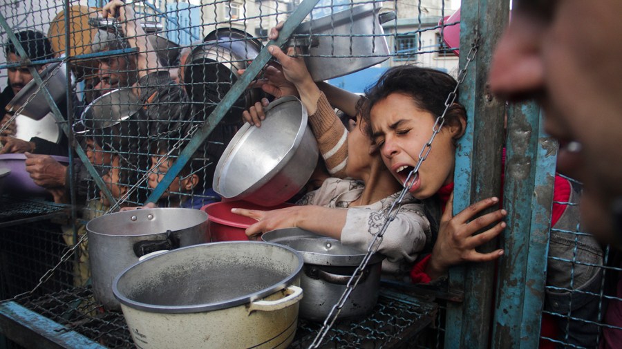 Palestinians line up with pots and containers to receive free meals at a refugee camp.