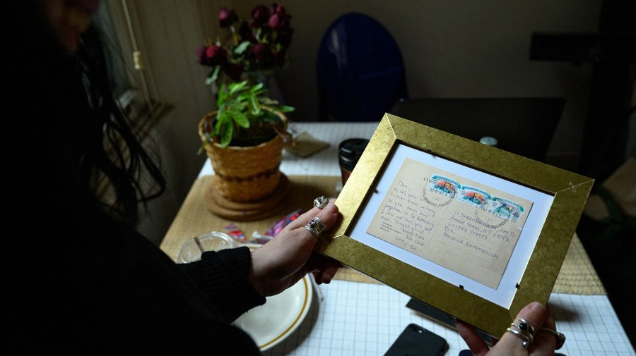 A woman holds up a framed postcard.