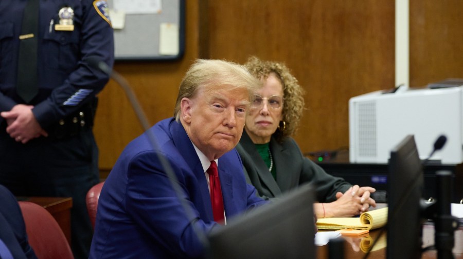 Donald Trump is sitting at a table with his lawyer Susan Necheles in the background.