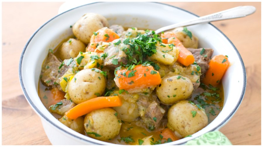 A spoon scoops out lamb stew with potatoes, onions and carrots.