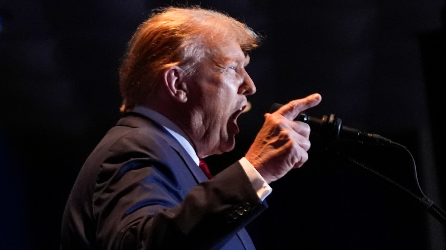 Former President Trump gestures while speaking in a microphone.