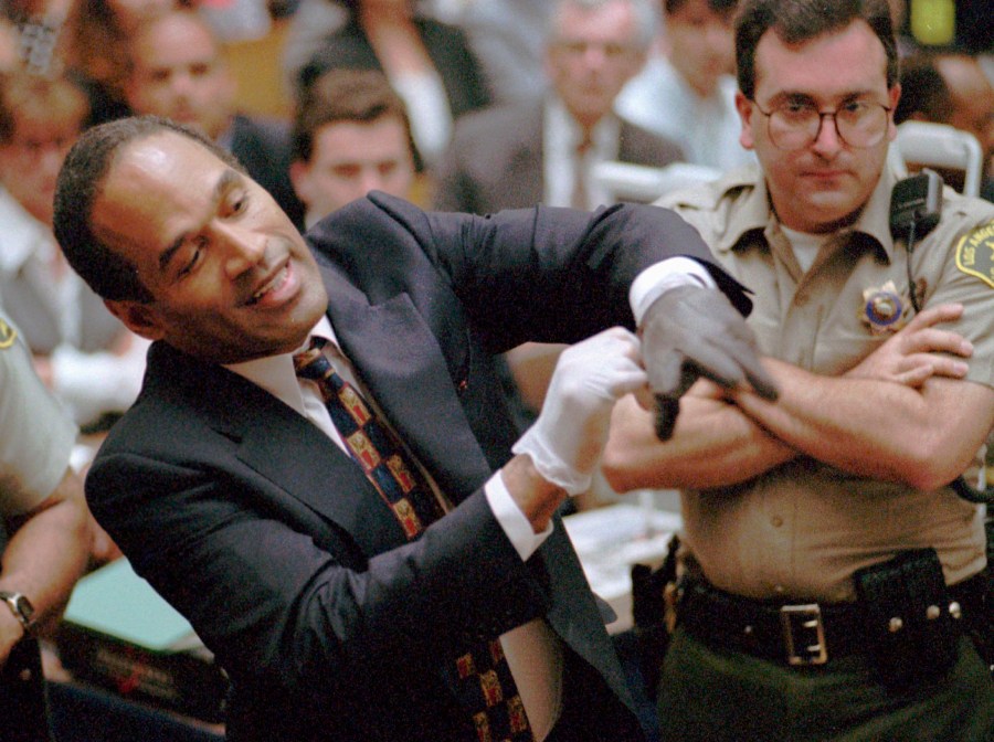 FILE - In this June 15, 1995 file photo, O.J. Simpson, left, grimaces as he tries on one of the leather gloves prosecutors say he wore the night his ex-wife Nicole Brown Simpson and Ron Goldman were murdered in a Los Angeles courtroom. Simpson, the decorated football superstar and Hollywood actor who was acquitted of charges he killed his former wife and her friend but later found liable in a separate civil trial, has died. He was 76. (Sam Mircovich/Pool Photo via AP, File)