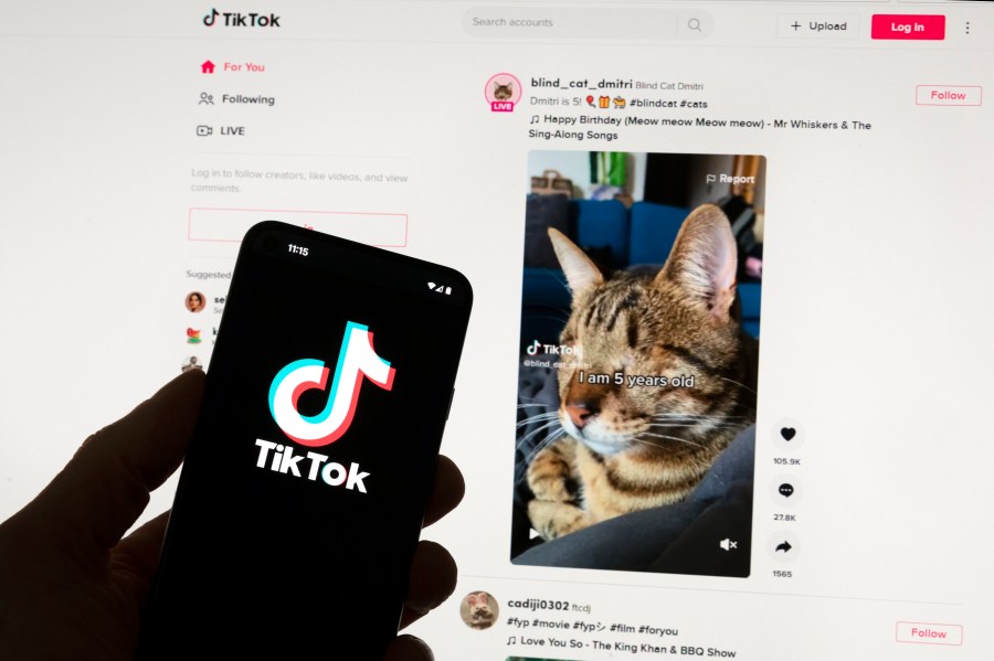 FILE - The TikTok logo is seen on a mobile phone in front of a computer screen which displays the TikTok home screen, Saturday, March 18, 2023, in Boston. European Union regulators said Wednesday, April 17, 2024, they're seeking details from TikTok on a new app from the video sharing platform that pays users to watch videos. (AP Photo/Michael Dwyer, File)