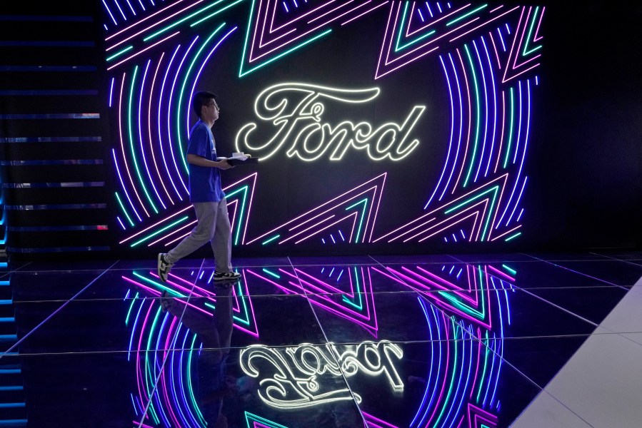 FILE - A worker walks past neon signs for Ford at the Auto Shanghai 2023 show in Shanghai, Tuesday, April 18, 2023. Ford reports their earnings on Wednesday, April 24, 2024. (AP Photo/Ng Han Guan, File)