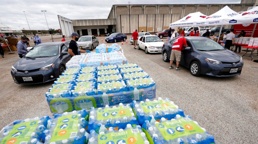 Volunteers distribute food and water bottles to drivers at a collection site.