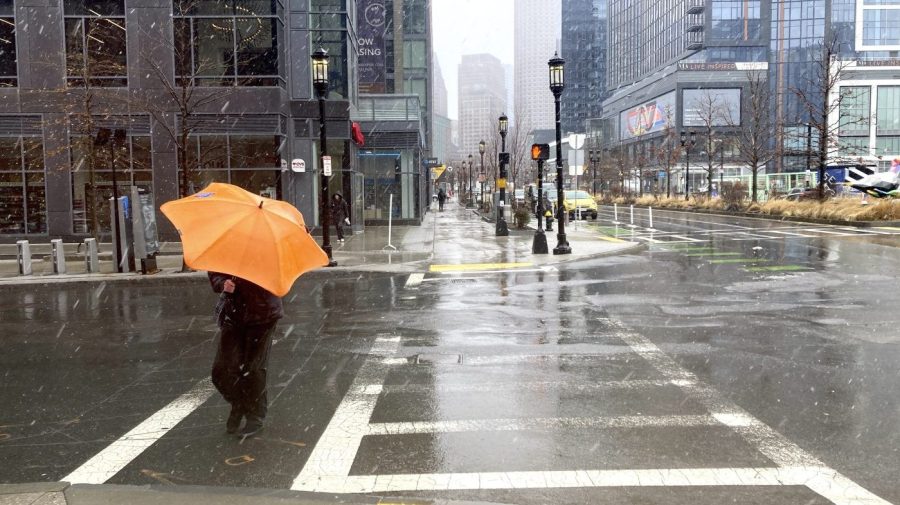 A person using an orange umbrella crosses a street during a storm.