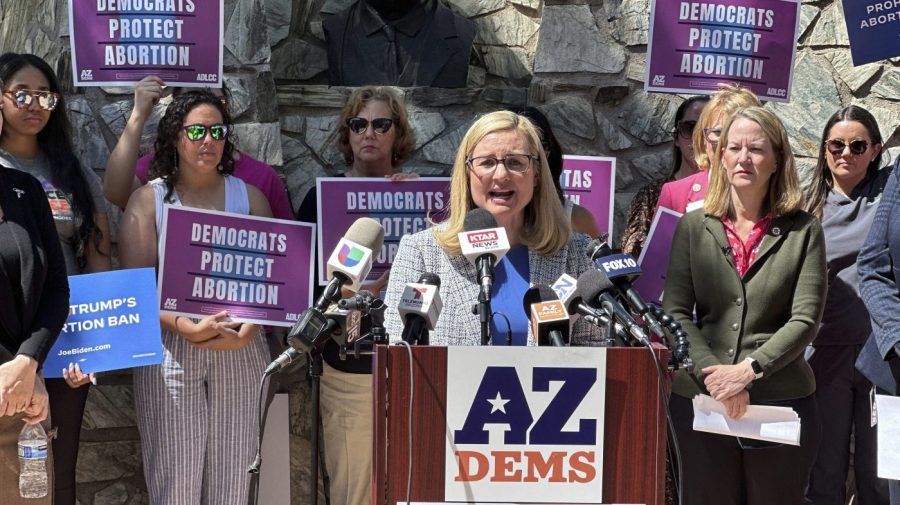 Kate Gallego speaks to reporters as abortion-rights advocates hold up signs in the background.